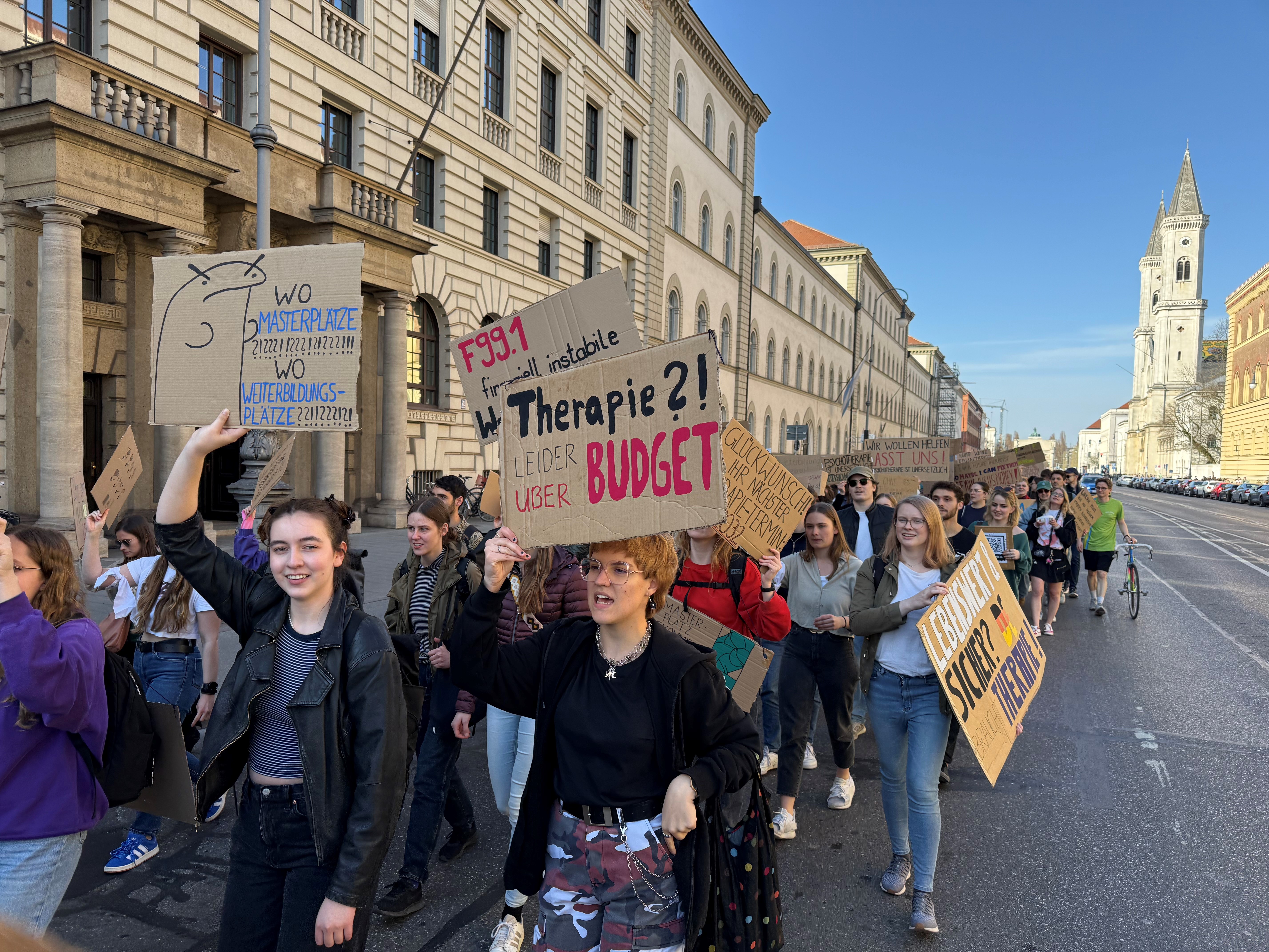 Demonstrierende laufen mit selbstgeschriebenen Plakaten und Schildern eine Straße entlang.